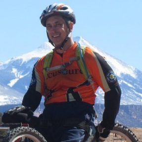 Lucian Smith seated on an accessible device in front of a snow covered mountain.